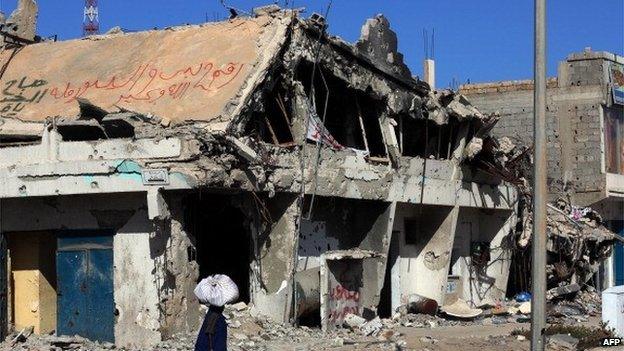 A Libyan woman walks past the rubble of a building in the Mediterranean city of Sirte on 13 October 2012