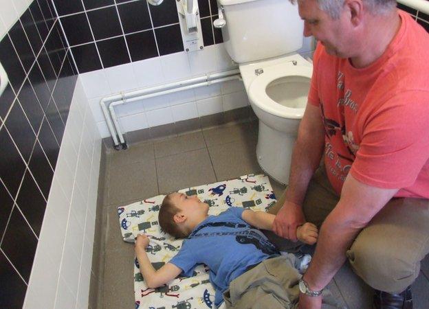 Alfie being changed on the floor of a toilet