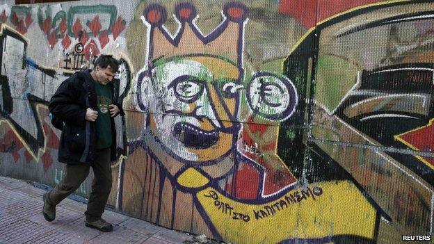 A man walks next to graffiti depicting a clown with a euro sign popping from his eye, in Athens 19 February 2015