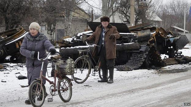 Residents pass a burned military vehicle in eastern Ukrainian city of Uglegorsk, not far from Debaltseve. 19 Feb 2015