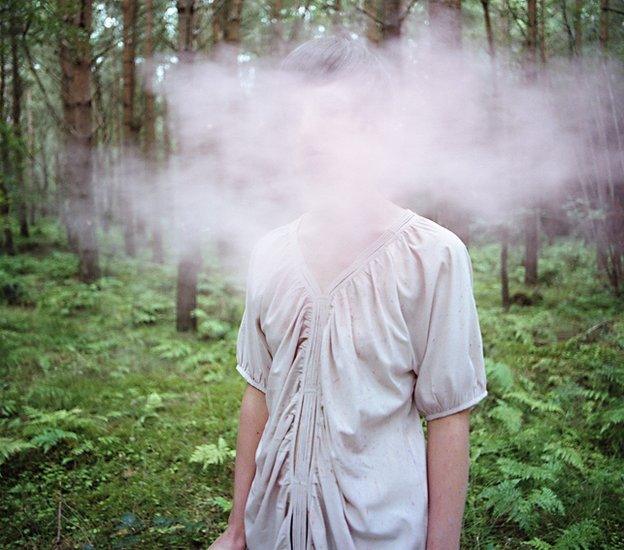 A woman in the forest, her face is completely covered by mist