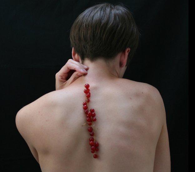 A woman naked holding cranberries down her back