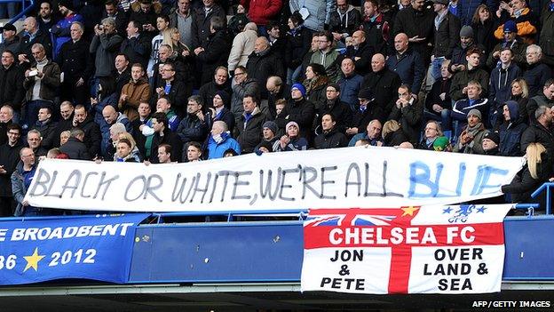 Fans holding a banner reading: "Black or white, we're all blue."