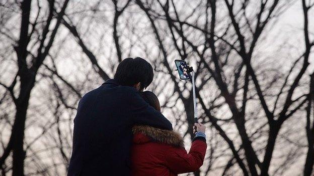 In a photo taken on November 26, 2014 a couple use a 'selfie stick' to take a group photo at a popular tourist spot in Seoul