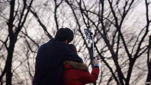 In a photo taken on November 26, 2014 a couple use a 'selfie stick' to take a group photo at a popular tourist spot in Seoul