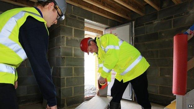 David Cameron tries his hand at carpentry with apprentice Kial Foye during a visit to the Barratt Homes Evolve development in Grays, Essex