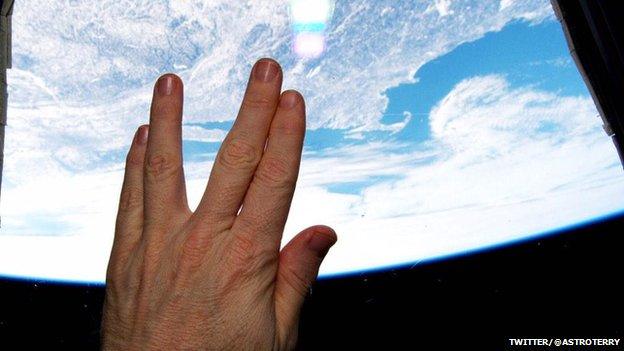 Hand giving a Vulcan salute, looking down at the Earth