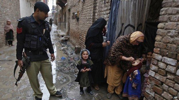 A police man watches on as a Pakistani health worker gives a polio vaccine to a child in Peshawar, Pakistan. 16 February 2015