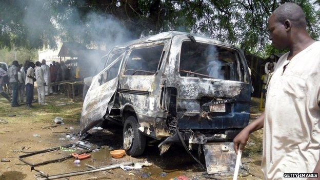 Residents stand near a smouldering remains of a bus targeted in a suicide attack in the northeast Nigerian town of Potiskum in February