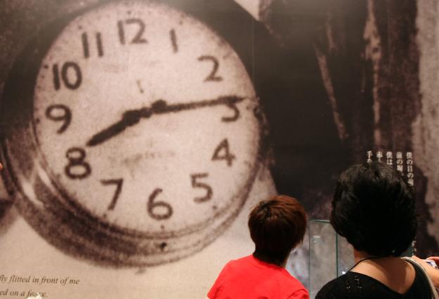 Visitors to a memorial at Hiroshima look at a picture of a clock broken at the moment the atomic bomb hit