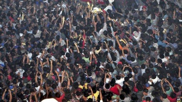 In this Thursday, March 5, 2015 photo, members of a mob raise their hands to take photos of a man, top centre, accused of rape after he was lynched and hung in the city landmark Clock Tower in Dimapur, in the north-eastern Indian state of Nagaland