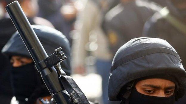 An Egyptian police officer holds a gun before a crowd of people.