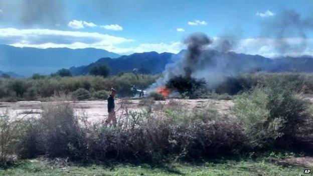 A man stands near the smoking remains of a helicopter that crashed with another near Villa Castelli in the La Rioja province of Argentina on Monday