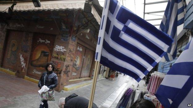 Greek flags fly as a tourist walks by a souvenirs shop in Athens on Monday, 9 March, 2015