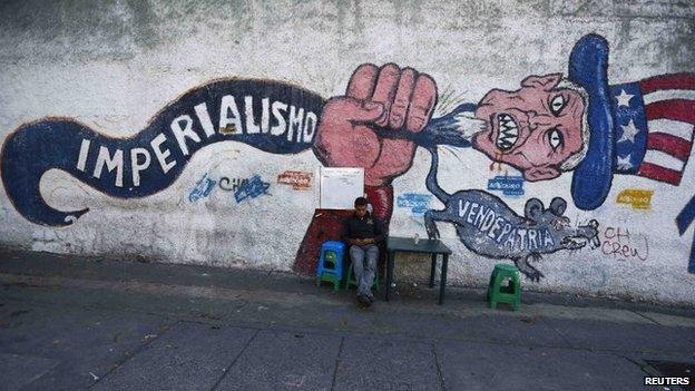 A man sits next to graffiti which reads "imperialism" and "traitor", in Caracas on 9 March, 2015.