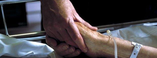 Close up of hand holding the hand of an elderly patient with an IV drip