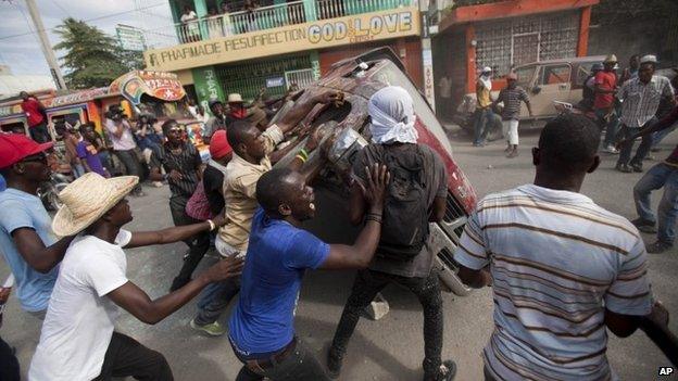 Demonstrators flip a car to block off a street during a protest demanding the resignation of President Michel Martelly in Port-au-Prince, Haiti