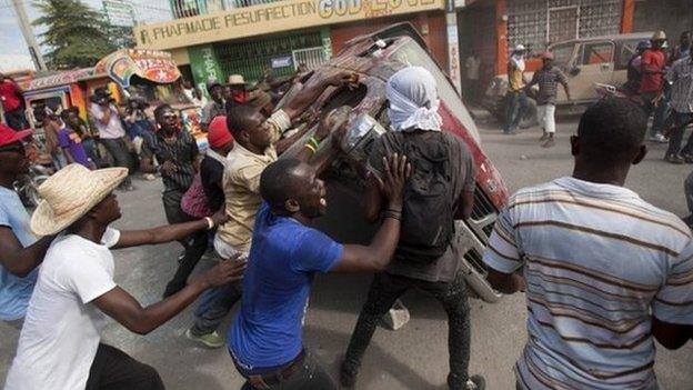 Demonstrators flip a car to block off a street during a protest demanding the resignation of President Michel Martelly in Port-au-Prince, Haiti