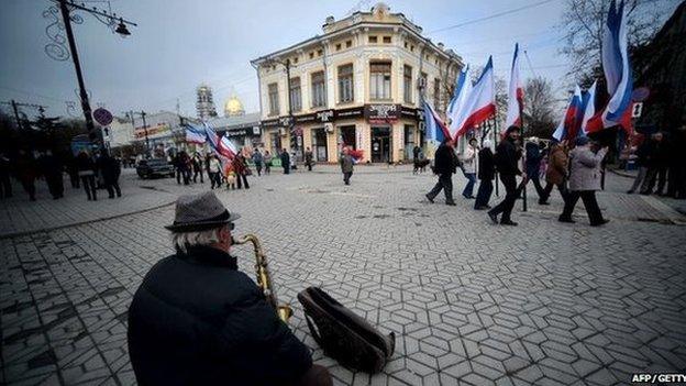 A man playing a saxophone as people waving Russian and Crimean flags walk to a pro-Russia rally in Simferopol's Lenin Square on 9 March 2014