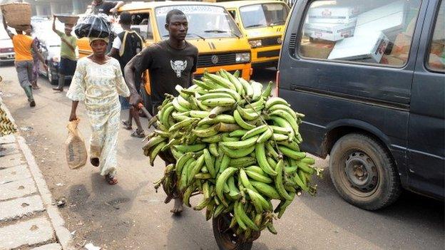 A woman accompanies a man carrying her plantain bananas to a car park at Mile 12 district in Lagos, Nigeria on 14 January 2012