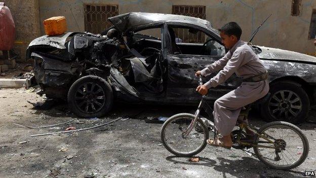 A Yemeni boy on a bicycle rides past a destroyed car in downtown Sanaa, Yemen, 21 March 2015,