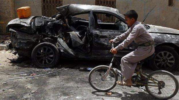 A Yemeni boy on a bicycle rides past a destroyed car in downtown Sanaa, Yemen, 21 March 2015,