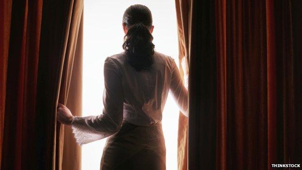 Woman looking through curtains