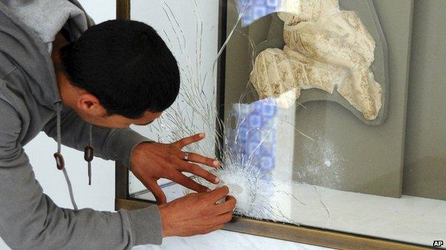 An employee of the Bardo Museum shows bullets marks on a glass of the Virgile room during the reopening day to the public of the National Bardo Museum in Tunis, Tunisia