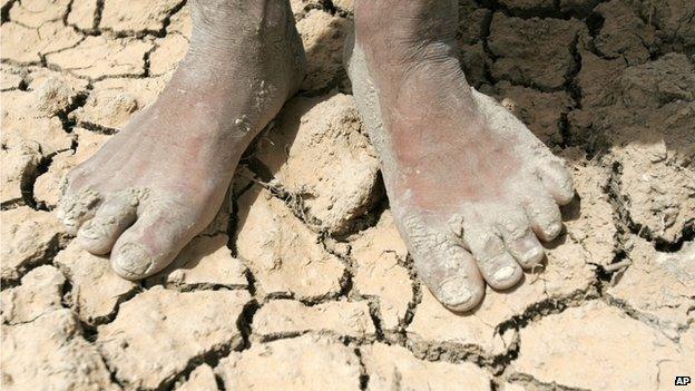 A boy stands on parched earth in a dry field on the outskirts of Najaf, Iraq