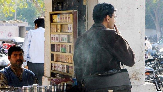 An Indian cigarette and tobacco products vendor looks on as one of his customers takes a puff on his cigarette in New Delhi