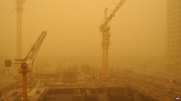 Migrant laborers, some wearing face masks, work on a construction site during a sandstorm in Dubai, United Arab Emirates, 2 April 2015.