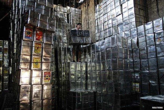 A labourer takes down tin boxes inside a tin container recycling factory in a slum area in Mumbai January 12, 2015.