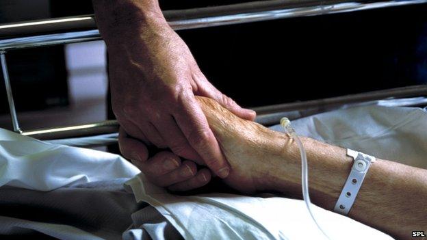 A nurse holds hand with an elderly patient in a hospital bed