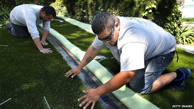 Juan Cruz and Juan Martinez, of the Onelawn lanscaping company, install a section of artificial lawn at a home April 3, 2015 in Burlingame, California.