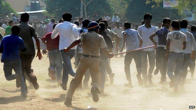 An Indian police office runs towards a crowd with his baton