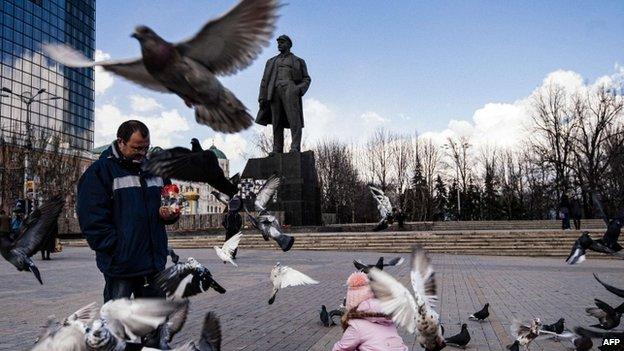 A man and a girl feed pigeons in front of a statue of late Soviet leader Vladimir Lenin on the central square in the city of Donetsk on 5 April 2015