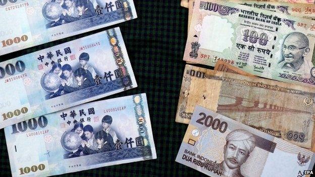 Taiwan dollar banknotes (L) lie lined up against banknotes of the Indian rupee and Indonesian rupiah on a table in Taipei, Taiwan, 13 April 2015