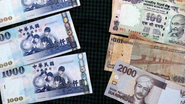 Taiwan dollar banknotes (L) lie lined up against banknotes of the Indian rupee and Indonesian rupiah on a table in Taipei, Taiwan, 13 April 2015