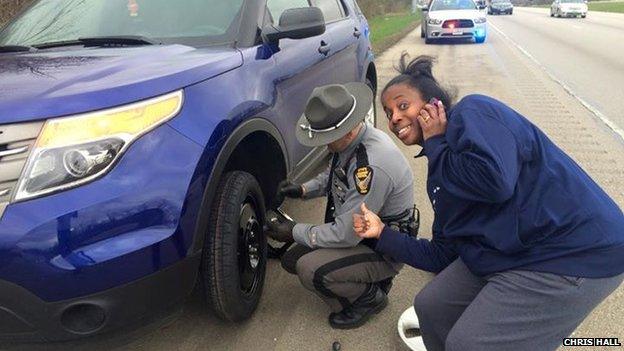 Picture of a white police officer changing a car tyre for an African American woman