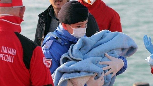 A Red Cross volunteer carries a baby wrapped in a blanket after migrants disembarked at the Sicilian Porto Empedocle harbor, Italy, 13 April 2015