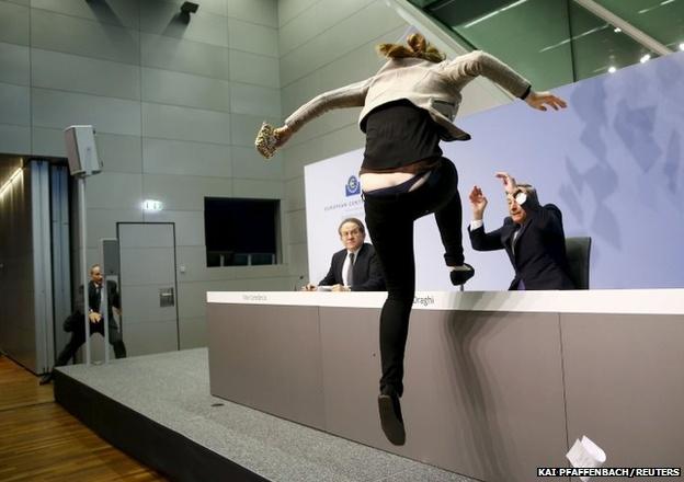 A protester jumps on the table in front of the European Central Bank President Mario Draghi