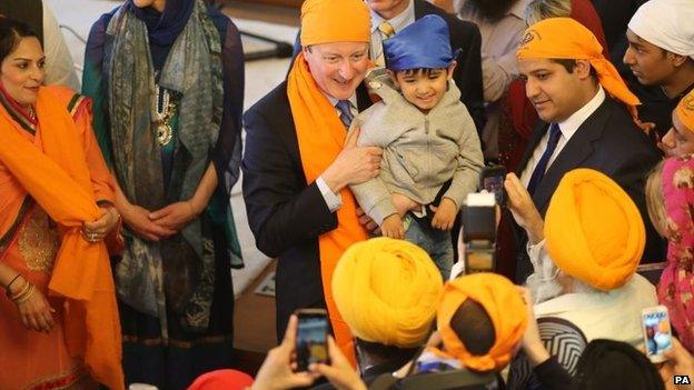 Prime Minister David Cameron holds a child on a visit to the Guru Nanak Darbar Gurdwara in Gravesend