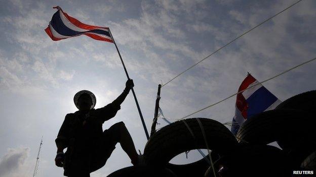 An anti-government protester holds a flag on a barricade as policemen gather in front of it near the Government House in Bangkok 18 February, 2014