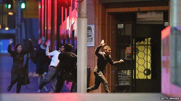 People run with their hands up from the Lindt Cafe, Martin Place during a hostage standoff on December 16, 2014 in Sydney