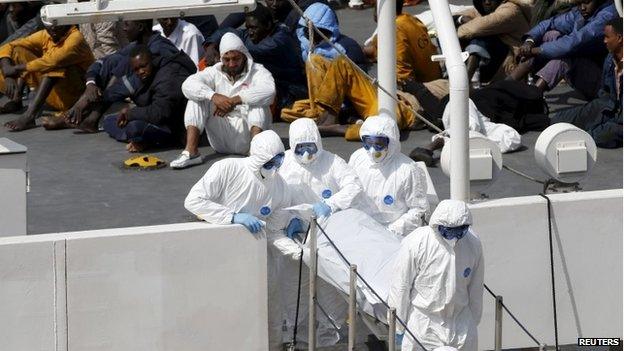 Armed Forces of Malta personnel in protective clothing carry the body of a dead immigrant off Italian coastguard ship Bruno Gregoretti as surviving migrants watch