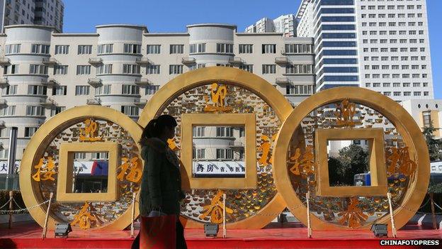 People walk past a copper coin-shaped decoration for Chinese New Year on January 20, 2014 in Zhengzhou, China.