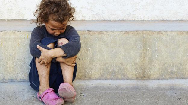 A child sitting on the floor beside a road