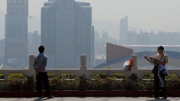 A man (R) reads a newspaper as an other one looks at the city's skyline in Shenzhen, 31 January 2007