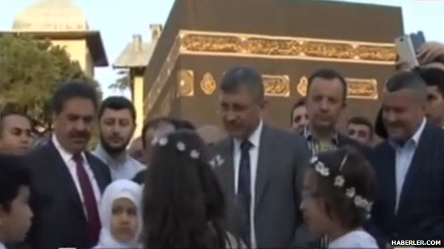 Hilmi Turkmen surrounded by people in front of the replica Kaaba