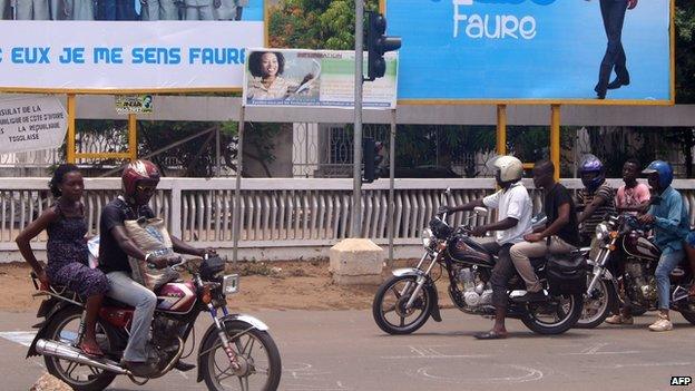 People ride motorcycles in front of posters of Togolese President Faure Gnassingbe on 11 April 2015 in the capital Lome.